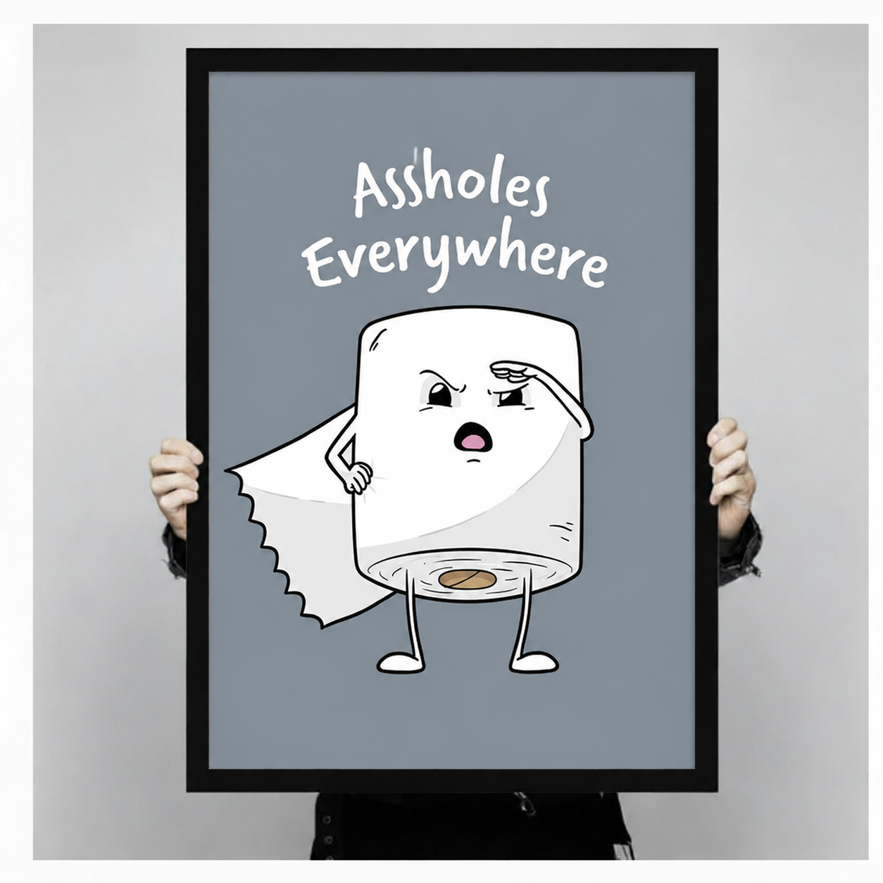 Person holding a large black-framed Assholes Everywhere toilet paper character art print showing size reference against a neutral grey background