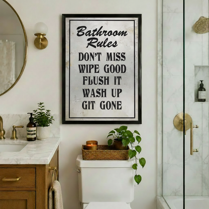 Black framed Bathroom Rules funny typography canvas art print with vintage distressed texture hung above a toilet in a luxury bathroom with gold fixtures round mirror and green plants