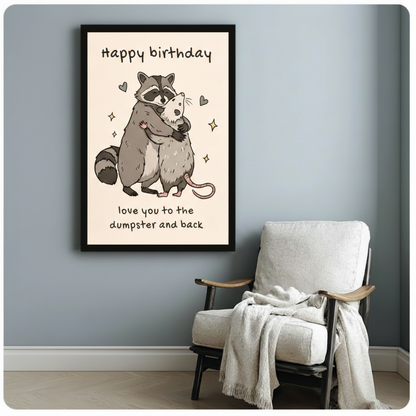 Black framed art print of a raccoon and opossum hugging with doodle hearts and stars, humorous birthday canvas wall art with love you to the dumpster and back quote on cream background, hung on a blue-gray wall beside a white linen armchair with a cream throw blanket