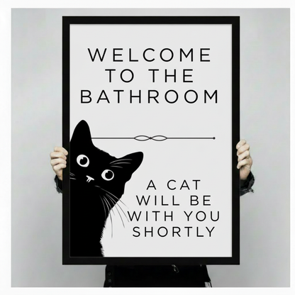 Person holding up large black-framed funny cat bathroom print showing Welcome to the Bathroom A Cat Will Be With You Shortly, demonstrating print size