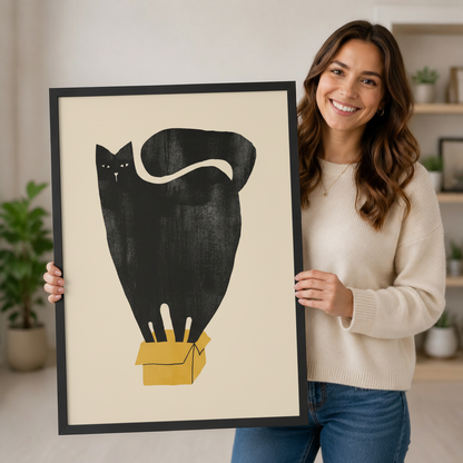 Smiling woman in cream sweater holding a large black framed minimalist black cat in yellow box wall art print in a bright home interior