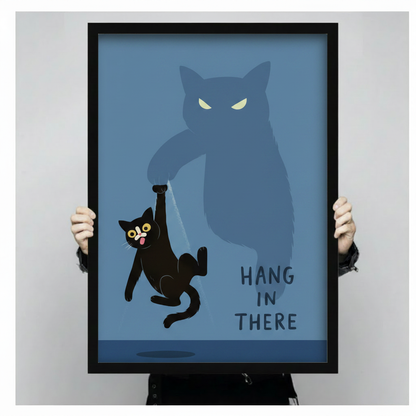  Both hands holding large framed "Hang In There" black cat print, full artwork view of cartoon cat with bulging eyes suspended by oversized shadow cat claw on steel blue background
