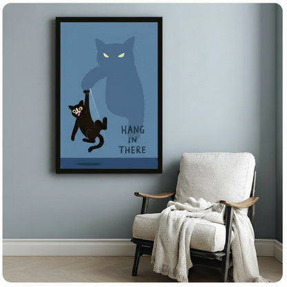 Whimsical black cat dangling helplessly from giant shadow paw, "Hang In There" funny cat wall art, black framed print beside white linen armchair with draped blanket in blue-grey reading nook