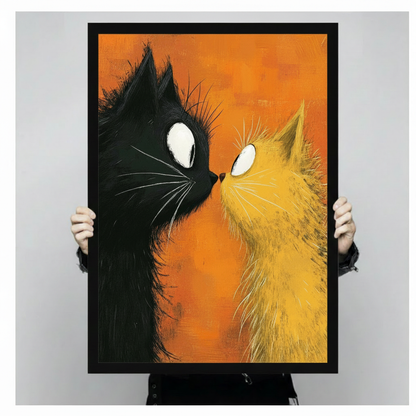 Hand-held framed canvas art print showing a close-up of a black cat and fluffy yellow cat facing nose to nose with bold white eyes on a textured orange background