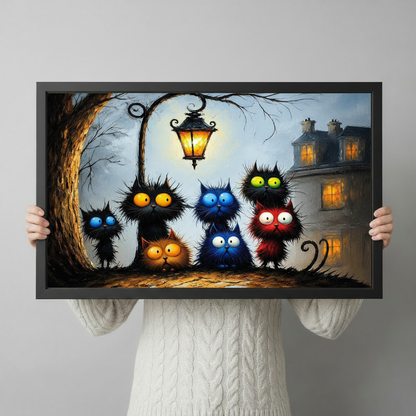 Person holding a framed art print of seven expressive black cats with oversized colorful eyes beneath an ornate street lamp against a moody twilight background