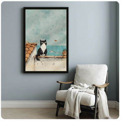 Black framed watercolor black and white cat on terracotta rooftop watching ocean canvas print beside white linen armchair on blue-grey wall - charming cat with dolphins and orange goldfish seaside wall art for reading nook or bedroom decor