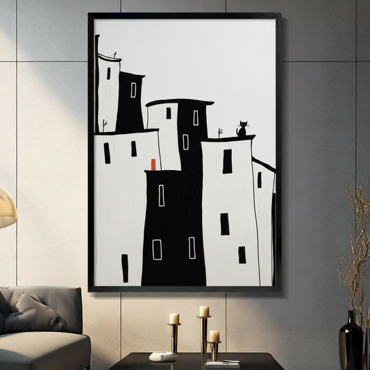 Black framed canvas print of minimalist black and white city buildings with black cat sitting on rooftop and red door accent, displayed on dark wall above console table
