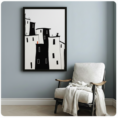 Black framed minimalist city skyline art print with whimsical black cat on rooftop and red accent window, styled beside white linen armchair in blue-grey room