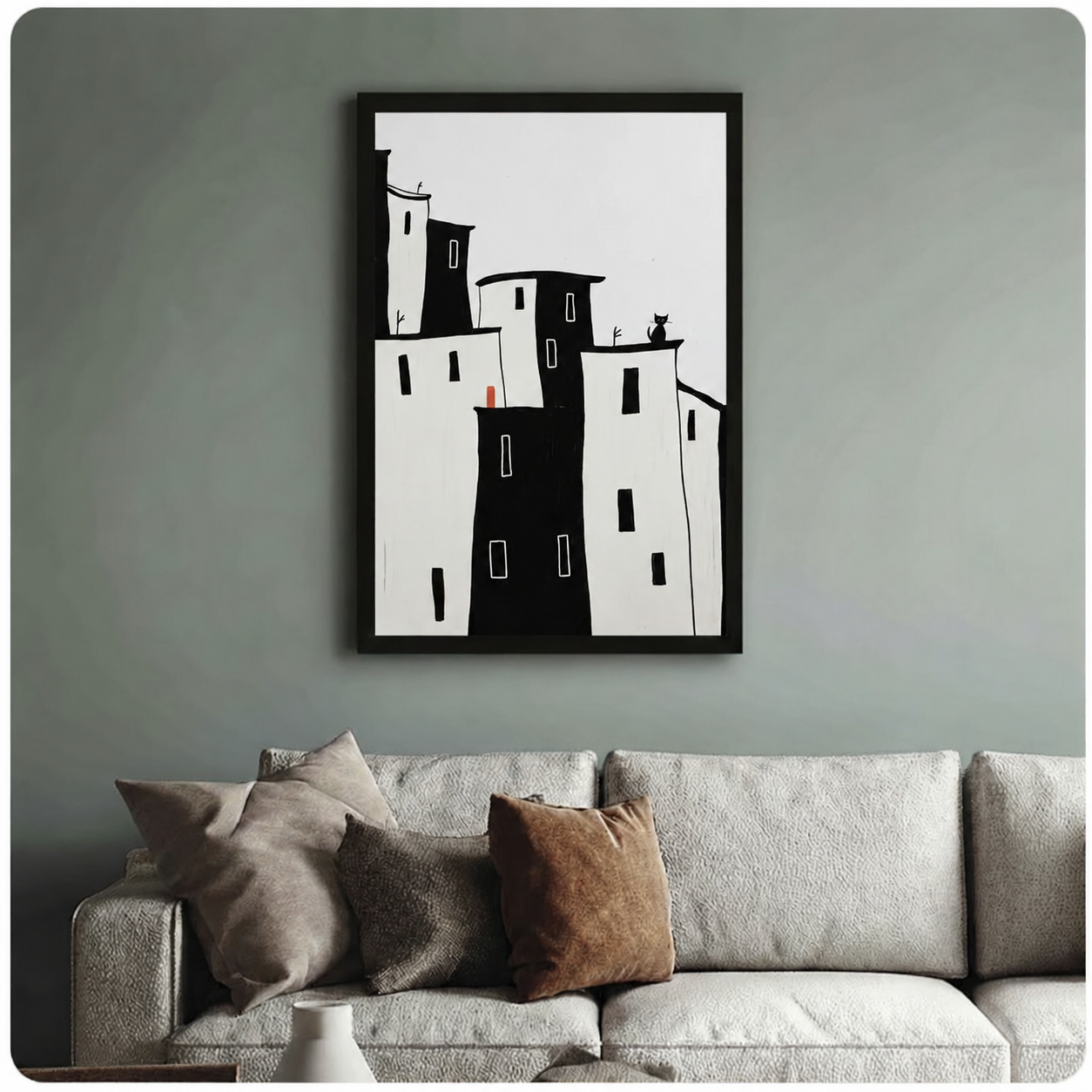  Framed minimalist wall art print of black and white cityscape with black cat perched on building rooftop and red door pop of color, displayed above sofa in sage green living room

