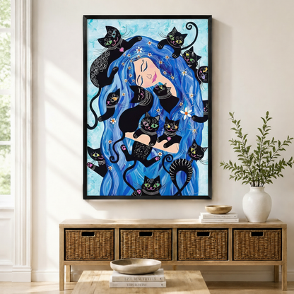 Black framed bohemian fantasy blue hair woman and black cats canvas art with a serene smiling woman with flowing cobalt blue wavy hair filling the canvas surrounded by eight playful decorative black cats with colorful eyes and intricate white patterned markings nestled throughout her hair alongside scattered white daisy flowers on a soft watercolor sky blue background, displayed above a wooden rattan storage bench with a white ceramic bowl, stacked books, and a white vase of greenery in a bright sunlit entr