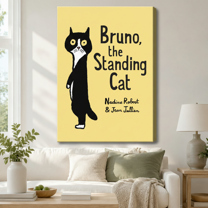 Stretched canvas wall art of a playful book cover illustration featuring a round-eyed black and white tuxedo cat standing upright with a startled expression beside the bold title Bruno the Standing Cat and script author names on a vivid lemon yellow background, hung above a white sofa with sage green and cream pillows and a ceramic table lamp in a bright airy living room