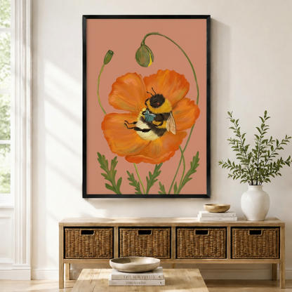 Framed botanical wall art print of a fluffy bumblebee resting inside a vibrant orange poppy flower on a dusty rose background, displayed above a wicker storage sideboard in a bright entryway