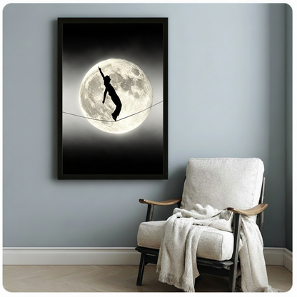 Black and white surreal photograph of a cat-girl silhouette with cat ears and tail balancing on a tightrope in front of a glowing full moon on a dark night sky wall art framed print beside linen armchair on blue-gray wall