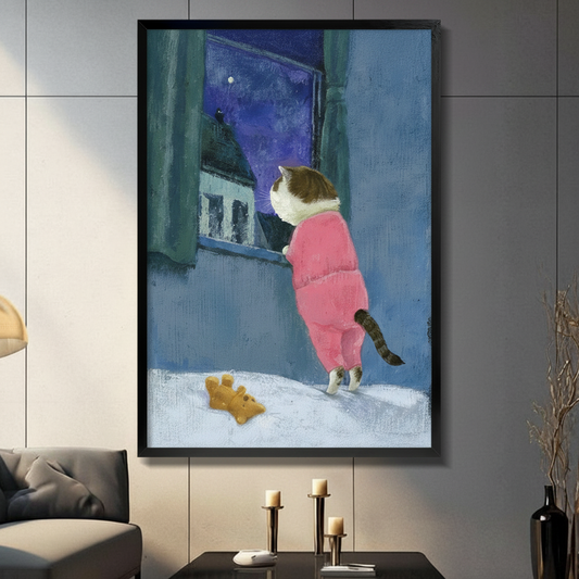 Framed wall art print of a chubby cat in pink pajamas gazing out a snowy window at the starry night sky, displayed on a dark grey wall above a console with candle holders