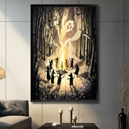 Black framed gothic dark fantasy Halloween illustration of nine black cat silhouettes dancing upright around a roaring bonfire with glowing ghost faces rising from the flames in a misty forest of bare branches and wildflowers canvas wall art on warm amber brown background displayed in a modern gray living room with dark sofa black coffee table and metal candlesticks