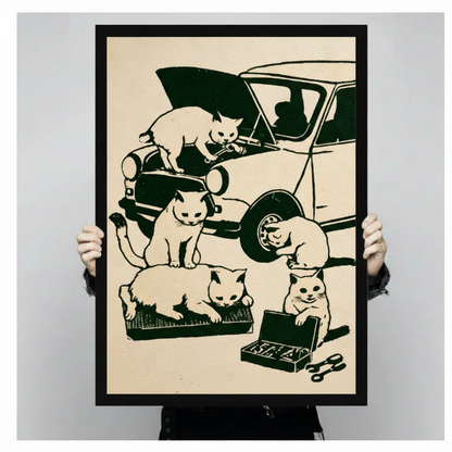 Two hands holding a large black framed retro vintage woodblock print of five white cats fixing a classic car with one on the hood holding a wrench one by the headlight one at the tire one on a parts tray and one smiling over an open toolbox funny cat mechanic canvas art print on warm cream background, front-facing vertical product size display