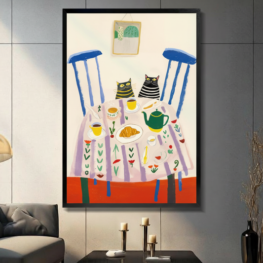Colourful illustration of two striped cats at a tea party table with croissants and a green teapot in a black frame, hung on a dark grey tiled wall above a console table with candle holders in a modern living room