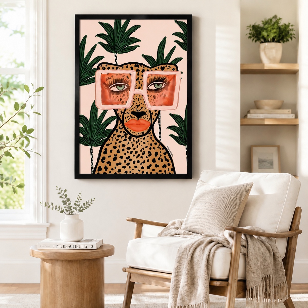 Bold cheetah portrait with oversized pink sunglasses and green palm leaves in a black frame, hung above a wooden armchair in a cozy neutral living space