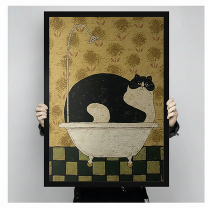 Close-up of a black framed art print showing a fat tuxedo cat sitting in a white clawfoot bathtub, surrounded by antique gold floral wallpaper and a dark green checkered tile floor, held by two hands