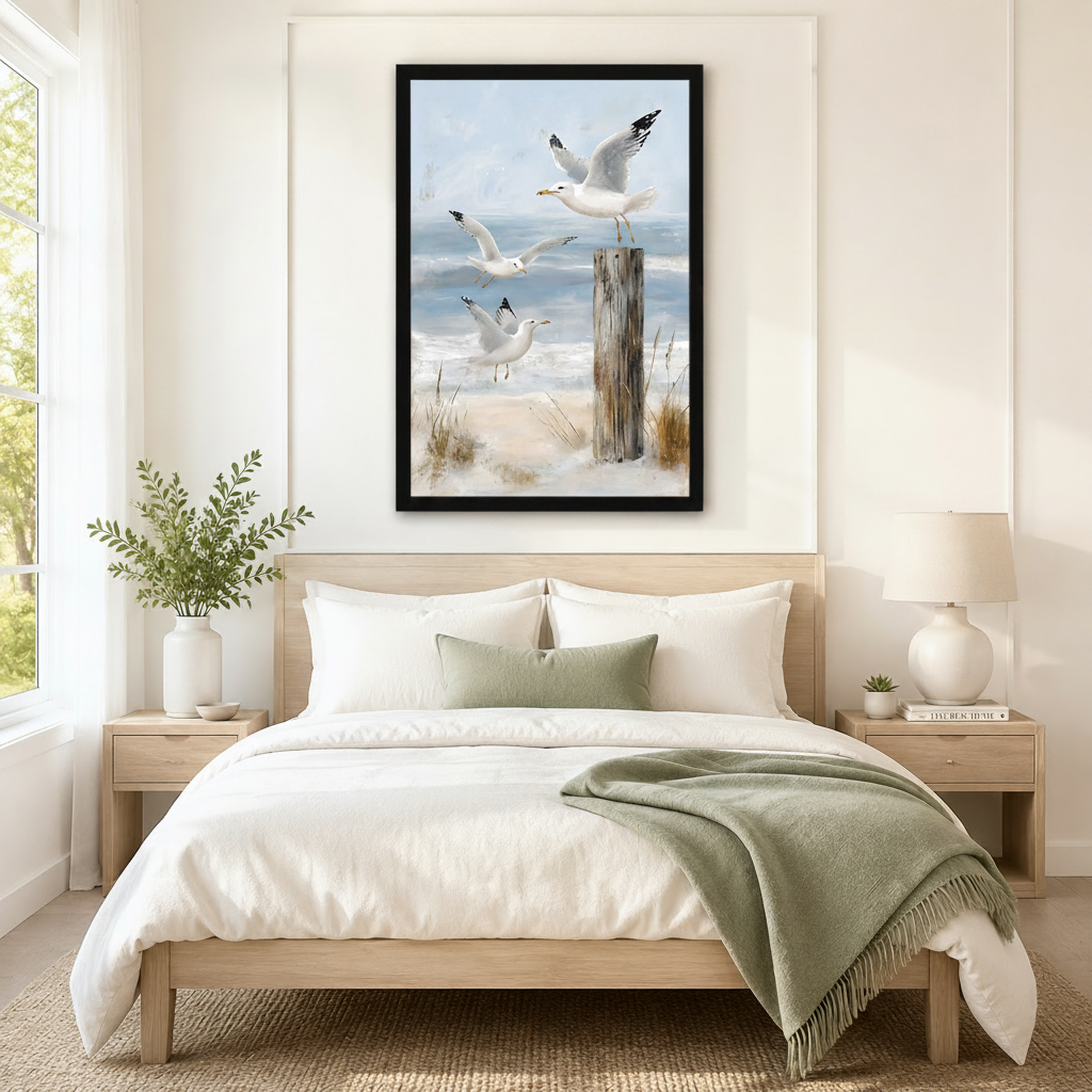 Framed coastal seagull wall art of three white gulls taking flight over sandy beach dunes and a driftwood post, displayed above a neutral linen bed in a calm Scandinavian bedroom