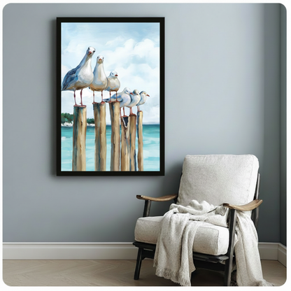 Black framed coastal seagull pier canvas art print with five white seagulls on wooden dock posts against a turquoise ocean and cloudy sky in realistic oil painting style on a blue-grey wall beside a white linen armchair