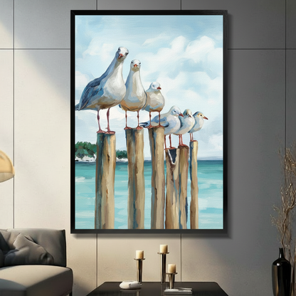 Framed coastal oil painting canvas wall art of five seagulls perched on wooden pier posts with turquoise ocean waves and fluffy white clouds displayed on a dark grey wall in a modern living room with candle holders