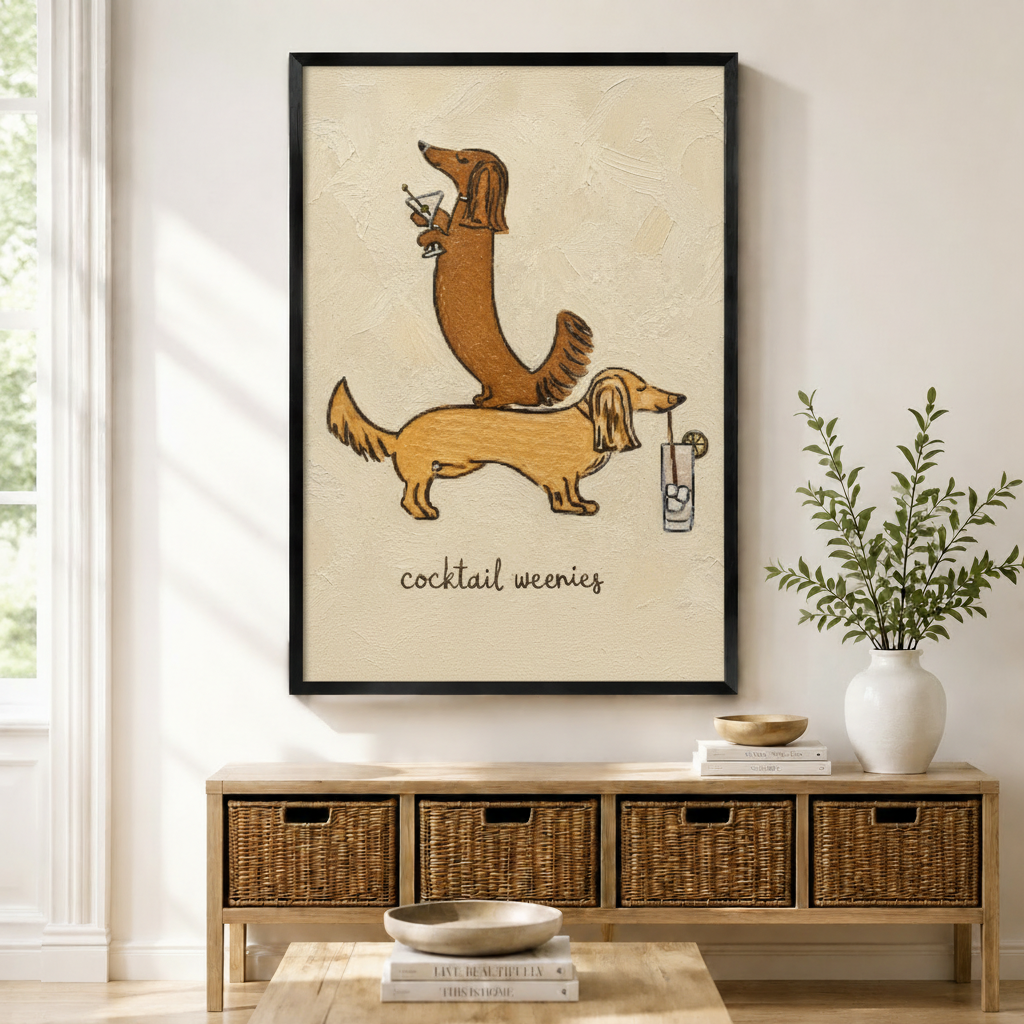 Black-framed canvas print of two whimsical long-haired dachshunds stacked together holding cocktail drinks with "cocktail weenies" lettering in textured oil painting style, displayed above a rattan storage console in a bright modern entryway