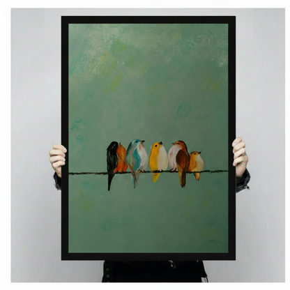 Person holding large black framed art print showing five colorful birds perched on a single wire against a muted teal green oil painting background