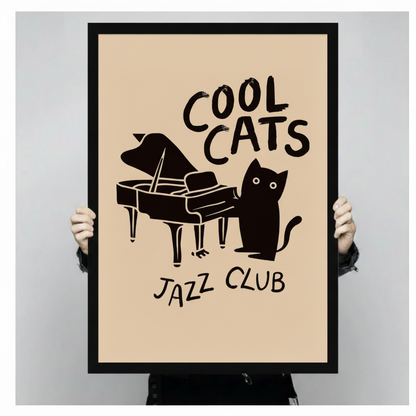 Hand-held framed wall art print showing a bold black cat standing next to a grand piano with "Cool Cats Jazz Club" brush-lettered text on a warm cream background