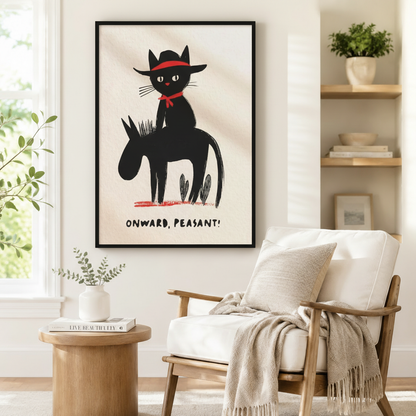 Large black framed humorous cowboy cat on donkey "Onward Peasant" wall art print beside a white upholstered wood-frame armchair with a linen throw blanket, round solid wood side table with a coffee table book, and open shelving with potted greenery