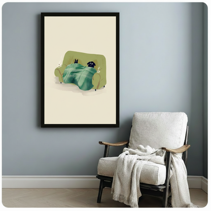 Black framed lazy cat and dog under a blanket canvas art showing a black cat and black dog lounging on a green couch sharing a teal throw with steaming mugs on either side against a soft cream background, displayed on a blue-gray wall beside a light upholstered wooden armchair draped with a cream knit throw blanket