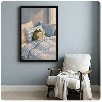 Black framed modern whimsical oil painting cute green bullfrog tucked in striped blue white bedding holding open book with both hands in soft sunlit bedroom scene canvas print on pale blue-grey wall beside white upholstered lounge chair with draped cream linen throw - charming reading frog in bed wall art for cozy reading nook decor