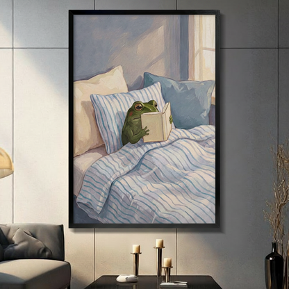 Framed modern whimsical oil painting green frog sitting up in bed reading book surrounded by blue and cream striped pillows under soft morning window light on muted blue-grey background canvas print on dark grey tile wall in modern living room with charcoal sofa and brass candlesticks - cozy reading frog in bed wall art for contemporary home decor