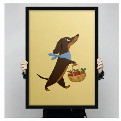 Illustrated dachshund canvas art in black frame held up against a light gray backdrop, showing a cartoon dog carrying a wicker basket filled with red apples