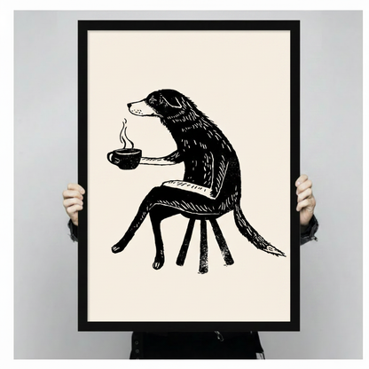 Two hands holding a large black-framed canvas print of a whimsical dog with coffee cup, showcasing print size and fine ink illustration detail