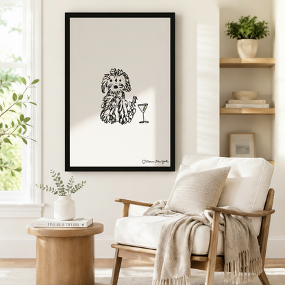 Black framed fluffy dog martini line art print hanging beside linen armchair in cozy minimalist reading corner
