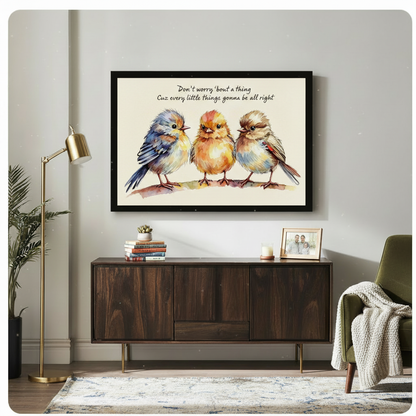 Whimsical watercolor of three cozy fluffy birds in blue orange and brown tones standing together on a branch with a hand-lettered inspirational lyric quote on a cream background charming bird quote wall art framed print above a dark wood sideboard with a gold floor lamp and green chair