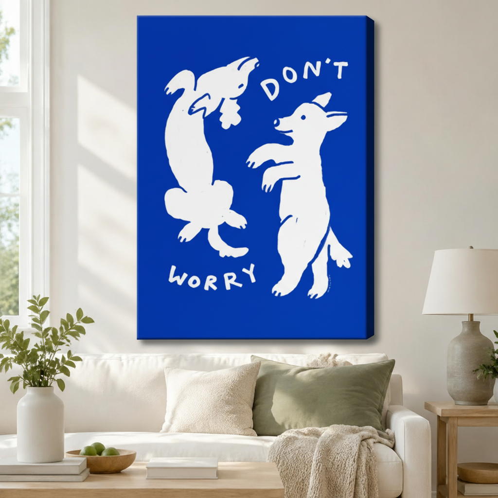 Stretched canvas wall art of two white dancing dogs on a bold cobalt blue background with "Don't Worry" text above a white sofa with sage green and cream cushions, a linen throw blanket, potted greenery, and a ceramic table lamp in a bright living room
