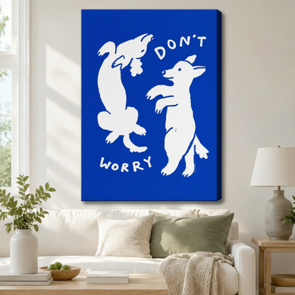 Stretched canvas wall art of two white dancing dogs on a bold cobalt blue background with "Don't Worry" text above a white sofa with sage green and cream cushions, a linen throw blanket, potted greenery, and a ceramic table lamp in a bright living room