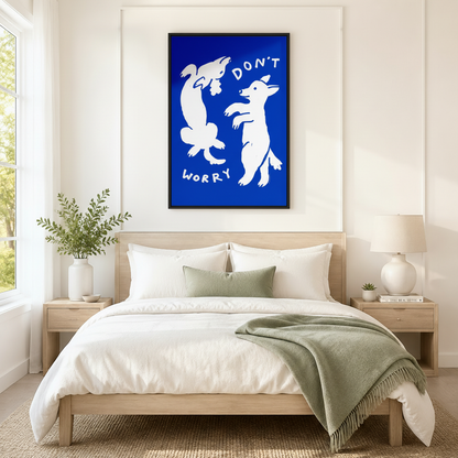 Black framed bold cobalt blue "Don't Worry" white dancing dogs wall art above a light oak bed with white linen bedding, a sage green fringed throw blanket, wooden nightstands, and a white ceramic table lamp in a bright Scandinavian bedroom