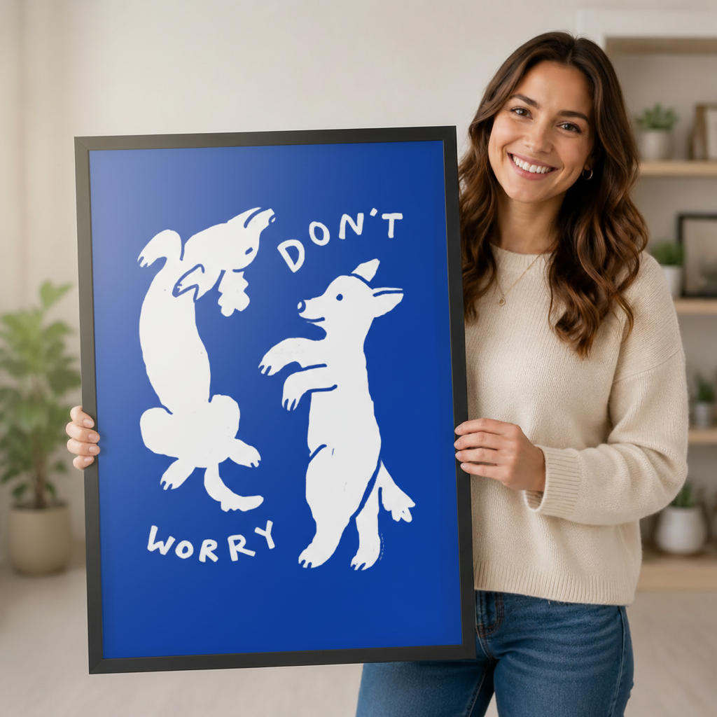 Smiling woman holding a large black framed bold cobalt blue "Don't Worry" white dancing dogs wall art print against a light gray backdrop with shelving and potted plants in the background