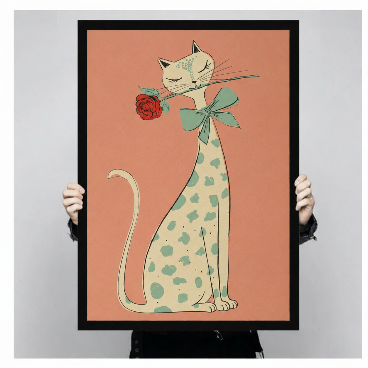 Elegant cat smelling rose framed art print held up to show full print size, peach background with green bow and red rose illustration detail