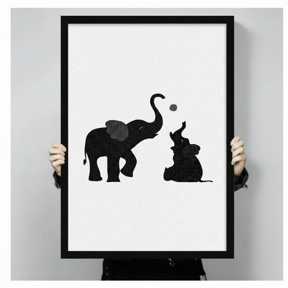 Hand-held display of black and white framed canvas art showing a mother elephant and baby elephant playing with a ball, minimalist oil painting style with textured finish