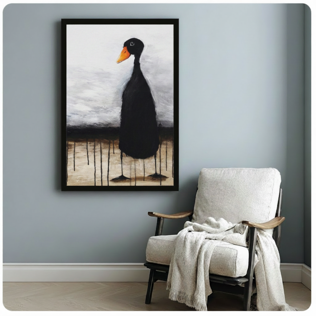 Black framed expressionist black duck with orange beak canvas art showing a lone elongated black duck with a vivid orange beak and small curious eye perched on impossibly thin legs with dark ink-like drips pooling at its feet on a moody layered gray and sandy beige oil-painted background, displayed beside a white linen wood-frame armchair with a cream throw