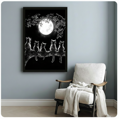 Gothic ink illustration of five cats with detailed fur texture sitting in a row on a tree branch looking up at a bright full moon with delicate white leaf branches arching overhead on a black background cat wall art framed print beside a white linen armchair with a cream throw blanket on a blue gray wall