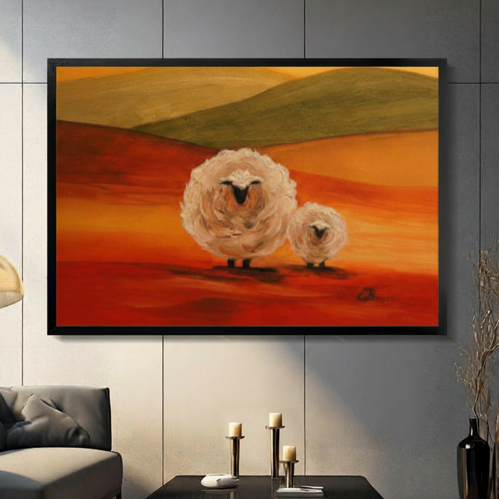 Black framed impressionist fluffy sheep duo at sunset canvas art with a large round woolly white sheep and a smaller lamb standing on a vivid red-orange rolling landscape beneath olive green hills and a warm golden amber sky in bold oil-paint style, hung on a gray panel wall above a dark gray sofa