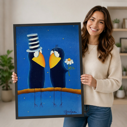 Smiling woman in a cream sweater holding a large vertical black framed whimsical folk art romantic crow couple canvas art print showing two plump dark navy blue cartoon crows on a warm branch facing each other, one with a tall black and white striped top hat and the other holding a white daisy, both with golden yellow beaks and white eye rings on a deep cobalt blue starry night background with gold sparkle dots in a bright plant-filled room