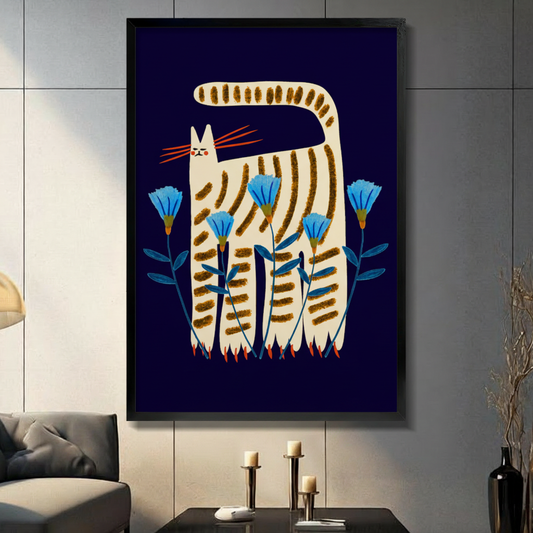 Framed folk art wall art of a whimsical cream striped cat with orange whiskers standing among blue cornflowers on a deep navy background, displayed in a modern dark grey living room
