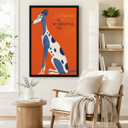 Black framed vintage French poster greyhound canvas art showing a tall slender blue and white spotted greyhound sitting elegantly with the handwritten L'élégance ne vieillit pas quote on a vivid orange background, displayed on a white wall beside a white wooden armchair with a cream fringed throw and a round wood side table with books