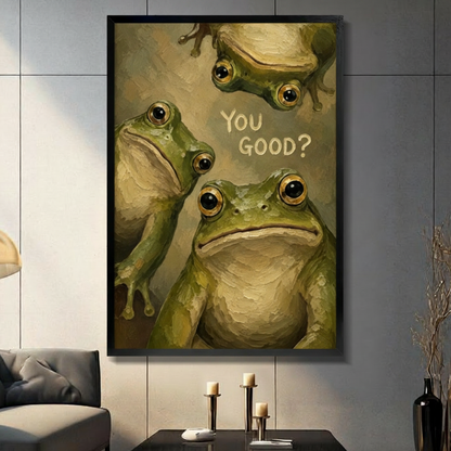 Black framed humorous oil painting of three green bullfrogs crowding the canvas with one hanging upside down at the top and a large frog staring directly at the viewer beside You Good hand-lettered text whimsical frog humor canvas wall art on olive gold background displayed in a modern gray living room with dark sofa and metal candlesticks